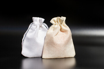 Two cloth bags on black background: white and beige textured fabric pouches