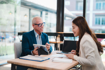 Senior manager using tablet explaining project to young businesswoman during a meeting in a modern...
