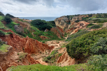 Obraz premium Scenic coastal cliff landscape with red eroded earth and vegetation