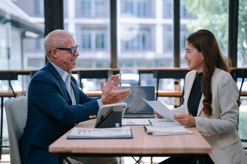 Senior manager explaining marketing strategy to young businesswoman during a meeting in a modern office, using a laptop, tablet and documents, discussing and collaborating on a project