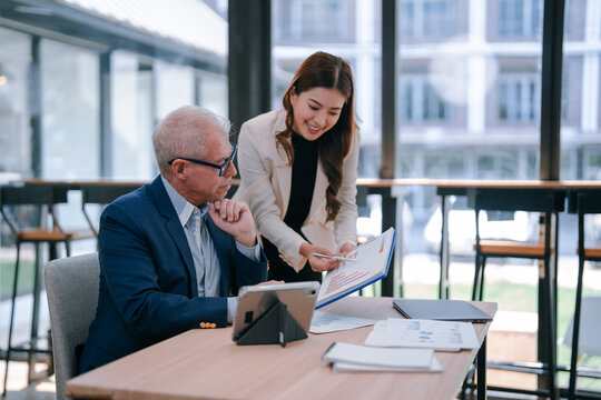 Senior businessman and young businesswoman are discussing graphs and using tablet in modern office, analyzing financial data and investment strategy