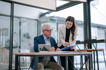 Senior businessman and young businesswoman are collaborating on a project, using a tablet and...