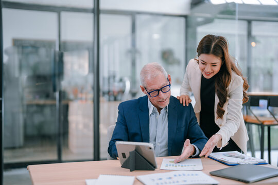 Senior businessman and young businesswoman discussing strategy using digital tablet and analyzing financial chart documents while working together in modern office