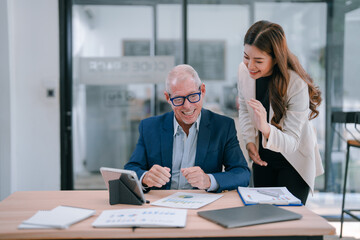 Happy senior manager and young assistant are discussing marketing data on digital tablet while working together on new project in modern office