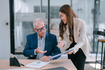 Senior male manager and young female assistant discussing company performance charts and reports in...
