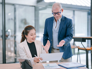 Senior manager coaching young asian businesswoman analyzing financial report in modern office,...