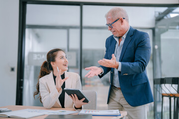 Senior male manager explaining marketing strategy to young businesswoman using tablet in modern...