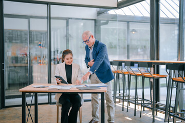 Senior male manager pointing at a financial report while guiding a young female businesswoman using...