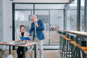 Senior manager pointing at a document and explaining project details to a young businesswoman...