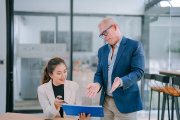 Senior manager engaging in a discussion about strategy with a young businesswoman, holding a folder...
