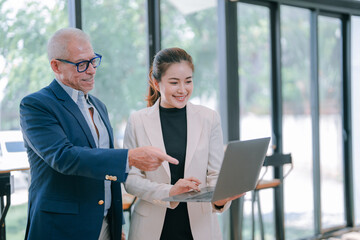 Senior caucasian manager pointing at a laptop held by his young female asian colleague, both...