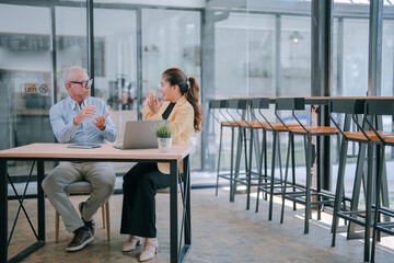 Senior manager explaining work strategy to a young businesswoman who is clapping hands, sitting at...
