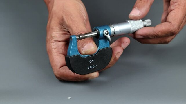 Hand holding analogue micrometer or diff micrometer, Calibration outside micrometer over grey background.
