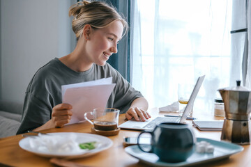  Gen Z woman working from home at cozy kitchen table with laptop and phone. Digital nomad lifestyle, mindfulness, remote work, balance, mental calm and modern freelancing