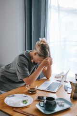  Gen Z woman working from home at cozy kitchen table with laptop and phone. Digital nomad...