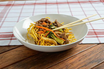 Enjoying a Colorful Plate of Stir-Fried Noodles With Vegetables and Beef on a Rustic Wooden Table