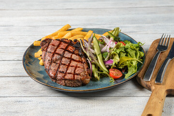 Savoring a Mouthwatering Grilled Steak With Fresh Salad and Crispy Fries on a Rustic Wooden Table