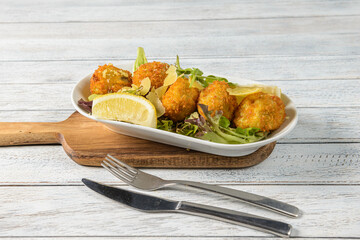 Golden Fritters Served on a Wooden Board Alongside Fresh Greens and a Wedge of Lemon for a Delightful Culinary Experience