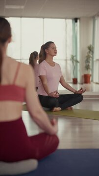 Women meditating in lotus pose during a yoga class in fitness studio.
