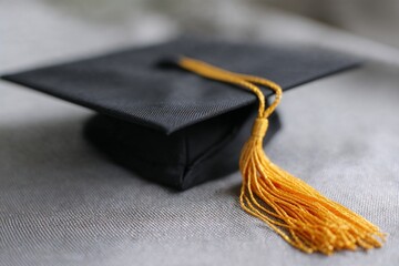 Black graduation cap with yellow tassel on grey fabric