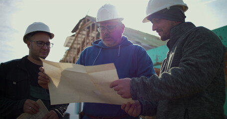 Construction workers reviewing blueprints at building site, teamwork in construction planning, industry professionals discussing project, collaboration in construction development