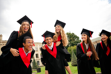 Joyous group of young graduates celebrate outdoors on a summer day in academic caps and gowns
