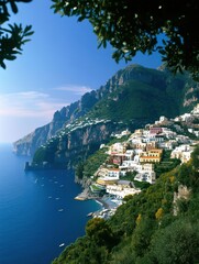 Naklejka premium Colorful cliffside buildings overlook a serene blue coastline with mountains rising in the background under a clear sky.