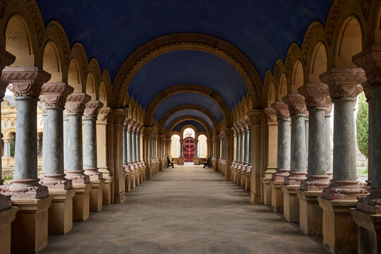 Interior of porticoed gallery at Derio Cemetery entrance, Spain, featuring marble columns and blue vaulted ceiling in Romanesque revival style