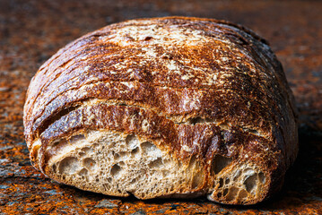 Freshly baked loaf of bread with a sliced-off piece on a corroded steel tabletop