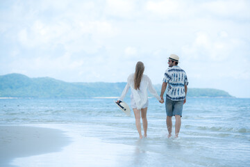Young couple on vacation on a white sandy beach, clear sky and sea