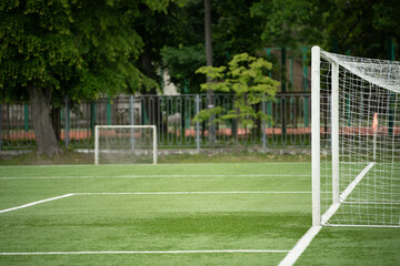 A well-maintained soccer field features a goal in the foreground under clear blue skies. Lush green trees surround the area, creating a vibrant atmosphere. Perfect for an afternoon match