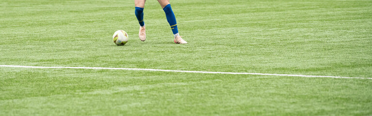 Fototapeta premium A soccer player stands poised to kick the ball on vibrant green artificial turf. The athlete is wearing blue shorts and socks, focused on the play during a competitive match