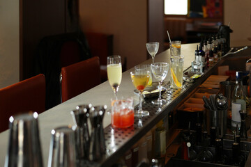 Bar counter with multiple cocktail glasses, some containing drinks, and bar tools, close-up