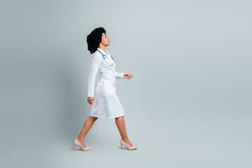 Qualified female doctor walking in uniform with stethoscope on a gray background, representing...