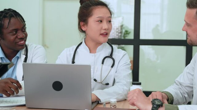 Medical professionals collaborating during strategy meeting, using digital devices like laptops and tablets while sharing insights in modern healthcare setting. Asian chinese female doctor talking