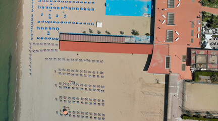 Aerial top-down view of a seaside beach resort with rows of umbrellas and sunbeds in summer