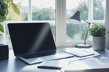 Cozy workspace featuring laptop, notebook, lamp, and plants by window