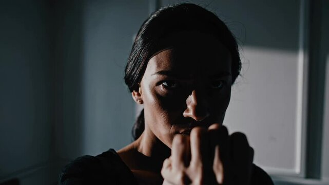 Intense focused woman shadowboxing in minimalist room with dramatic lighting