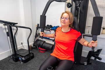 Mature woman doing bodybuilding exercises for the torso on a weight machine at home.