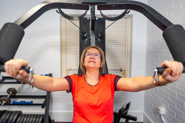Mature woman doing bodybuilding exercises for the chest with a weight machine at home.
