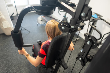 Woman on her back doing strength exercises with a weight machine in her home gym.
