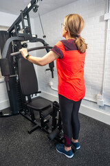 Mature woman on her back doing strength exercises with a weight machine in her home gym.