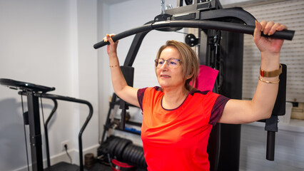 Mature woman doing bodybuilding exercises for the torso on a weight machine at home.