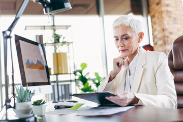 Professional mature businesswoman working in an elegant office setting analyzing data with determination showcasing leadership