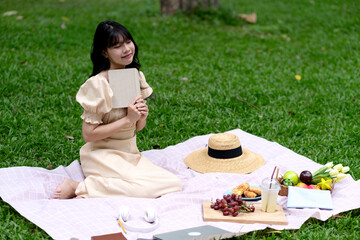 Smiling woman with book are sitting on the green grass in the park