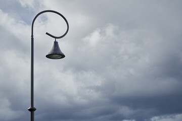 Minimalist composition featuring a uniquely curved black street lamp standing against a moody sky filled with dense clouds, capturing a coastal atmosphere and dramatic natural lighting.