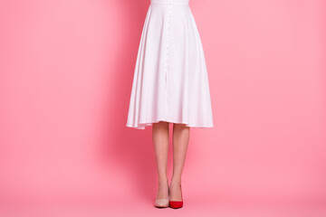 Elegant young woman in white dress and mismatched shoes standing against a pink background exuding...