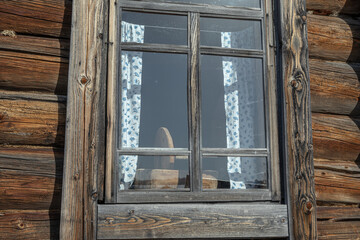 An old wooden log house built in the 19th century. Windows in a rustic house with fabric curtains . Life in the countryside. The history and traditions of rural life.