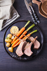 Lamb chops with carrots and potatoes, black background. Roasted rack of lamb. High angle view