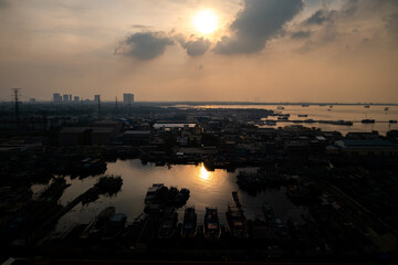 A hazy sunset casts an orange glow over a crowded harbor and city skyline, evoking a somber, industrial atmosphere